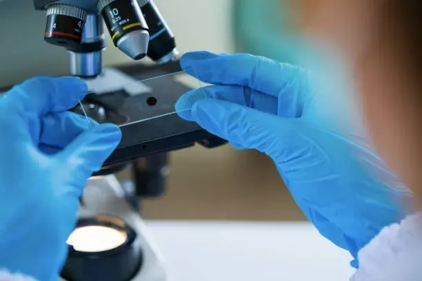 A laboratory pathologist analyzing a sample under a microscope for cytopathology evaluation